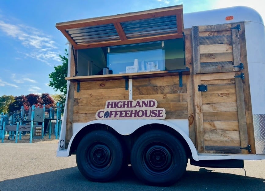Highland Coffeehouse mobile trailer with wooden exterior, open window counter, and dual wheels parked at an outdoor venue